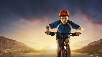 Portrait of young boy in helmet and uniform riding road on bike. Mountain landscape