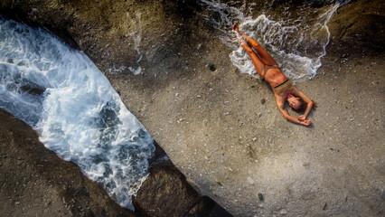Woman in bikini relaxes on a rock in a Mediterranean island