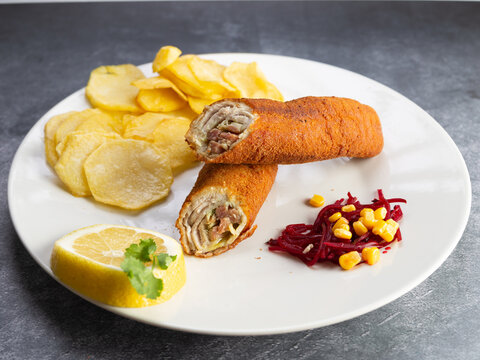 flamenquin with potatoes and lemon garnish, typical Spanish food stuffed with loin and ham, on a white plate on a cement background