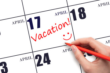 A hand writing a VACATION text and drawing a smiling face on a calendar date 17 April. Vacation...