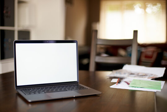 Mockup image of laptop with blank white desktop screen on a wooden table in an ordinary apartment. Business papers lie near the laptop in the home office. Laptop with blank screen for design.