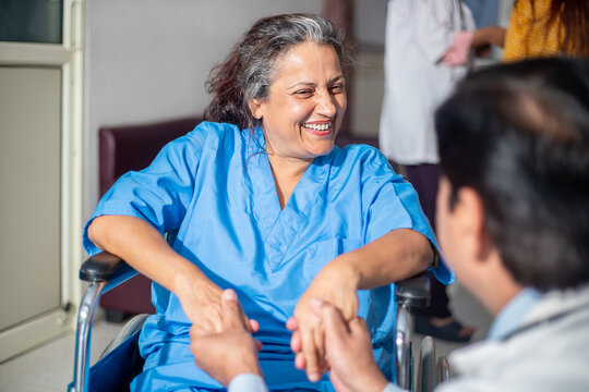 Happy indian elderly female patient looking at doctor in hospital ward while sitting on wheel chair, Old people healthcare concept.