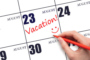 A hand writing a VACATION text and drawing a smiling face on a calendar date 23 August. Vacation planning concept.