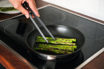 man frying asparagus in a frying pan on the stove close-up