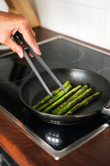 man frying asparagus in a frying pan on the stove close-up