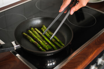 man frying asparagus in a frying pan on the stove close-up