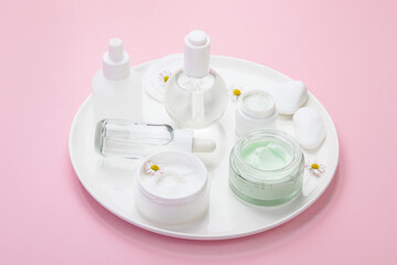 Face and body care products assortment on pink background.