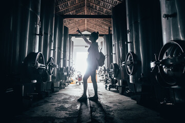 Young woman in a wine cellar pointing to the vats with light in the background © Dani Palazón
