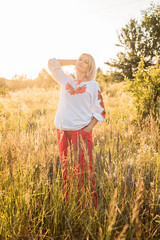 Naklejka na ściany i meble portrait of happy joyfull mature woman wearing traditional Ukrainian embroidered shirt - vyshyvanka in countryside during beautiful sunset