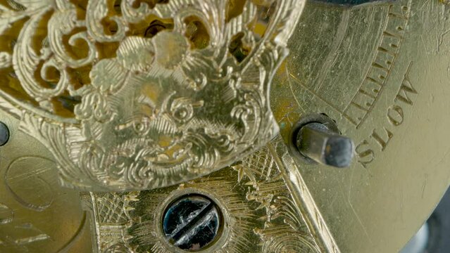 Clockwork mechanism macro. Round wheel with a carved pattern from curlicue on an antique gold clock. Old vintage clockwork working. Internal movement of watch with rotating spring and screws.