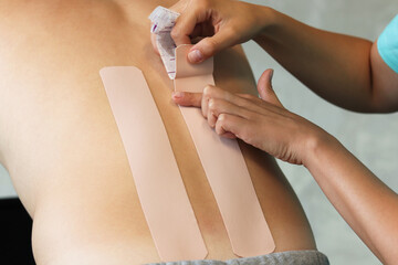 Physical therapist applying kinesio tape on male patient's lower back. Kinesiology, physical therapy, rehabilitation concept.