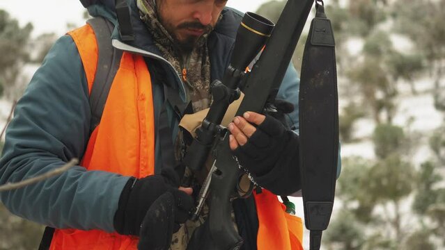 A hunter man with facial hair checks his rifle to see if it is loaded while standing outdoors on a cold day, close up medium shot