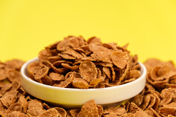 Durum wheat flakes - quick breakfast cereal on a plate on a yellow background, space for text.