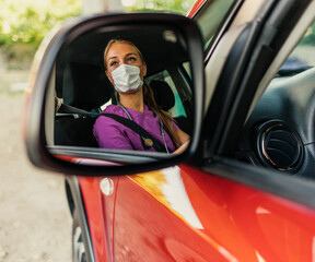 Reflection in rear-view mirror of doctor woman wearing face mask while sitting inside of a car. Health Worker, transportation and people concept.