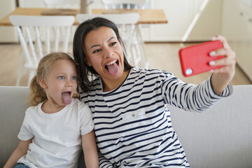 Affectionate mother and kid are taking selfie. Young european mum makes photo with little daughter.