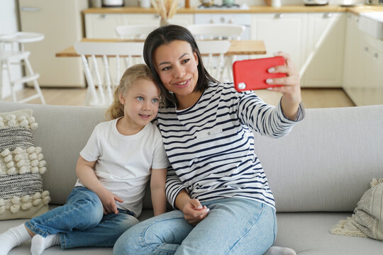 Mom, foster daughter use phone chat with father by videocall or take selfie sitting on couch at home