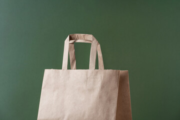 Kraft paper recycled shopping bag on green background minimal concept. Sustainable packaging concept.