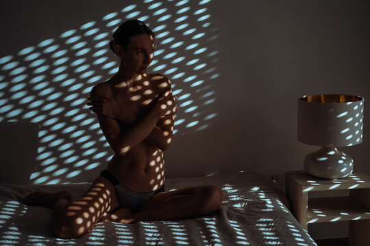 Portrait of a beautiful nude woman posing under a patterned shadow. Beauty of female body concept.
