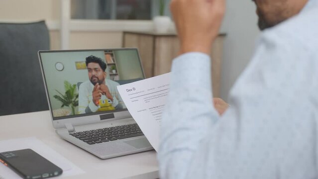 Recruiter busy taking online or virtual interview of applicant by seeing resume at office - concept of job, employment or consultation.