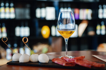 Glass of white wine and appetizer of mozzarella and ham.