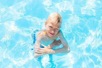 Fototapeta na wymiar happy baby boy swimming in the blue water pool, the concept of summer holidays and school holidays