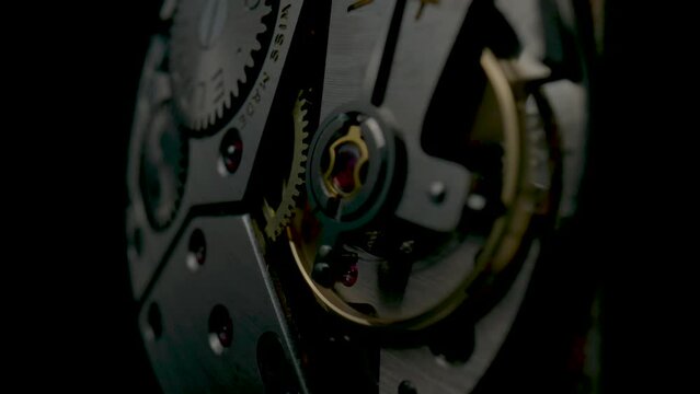 Disassembled vintage pocket watch with clockwork turning on black isolated background. Working clock mechanism with rotating spring, gears, gearing and toothed wheels. Close up.