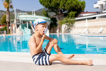 happy baby boy by the pool with water slides eating ice cream in the summer, the concept of a...