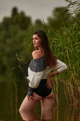 Naklejka na ściany i meble Attractive young brunette in a sweater and and black pantians posing on the reeds beach. Beach fashion, seductive woman resting near the water