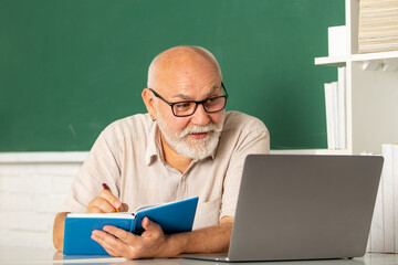 Portrait of senior teacher teaching line of high school students with notebook in classroom on...