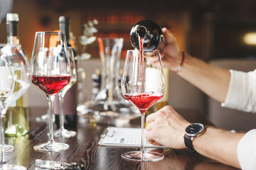 Faceless sommelier pours red wine into stem glass.
