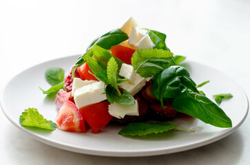 Vegetarian salad with tomatoes, cheese, strawberry, basil and mint on the white plate stock photo