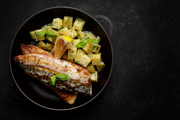 Grilled mackerel fish fillet, in a pan with boiled potatoes, on a dark background