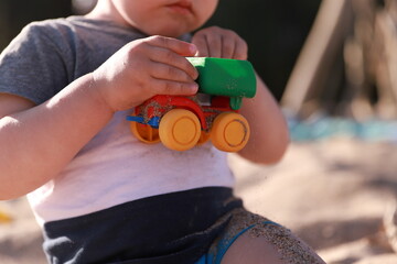 A little boy plays with a colorful toy car on the beach, sandy shore of the lake, river, sea