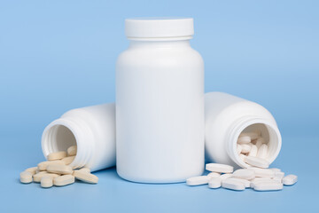 White medicine bottles, one closed and two with pills spilled on blue background with copy-space