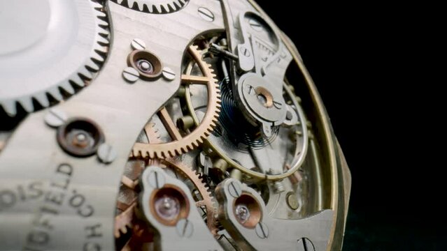 Macro shot of the internal parts of antique pocket watch. Clockwork with rotating spring, gears, cogwheel and wheels with tootheds on isolated black studio background. Disassembled silver watch.