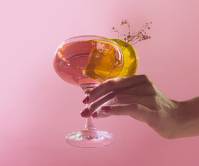 Female hand rising glass of delicious alcoholic cocktail with rose water and sparkling wine isolated over pink background