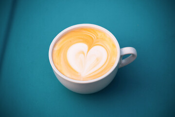 Cup of cappuccino with heart on a blue surface