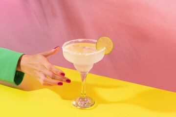 Female hand taking glass of delicious margarita cocktail isolated over pink yellow background