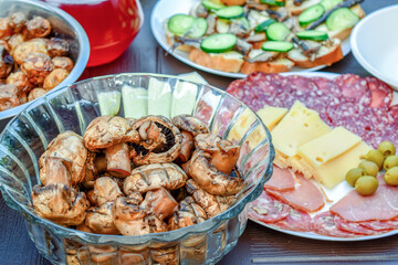 Grilled mushrooms in a transparent bowl, cold cuts and sandwiches, picnic