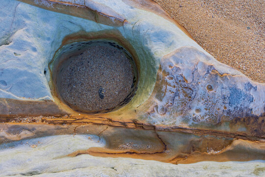 Close up detail of a circular pool filled with sand in a multi coloured rock
