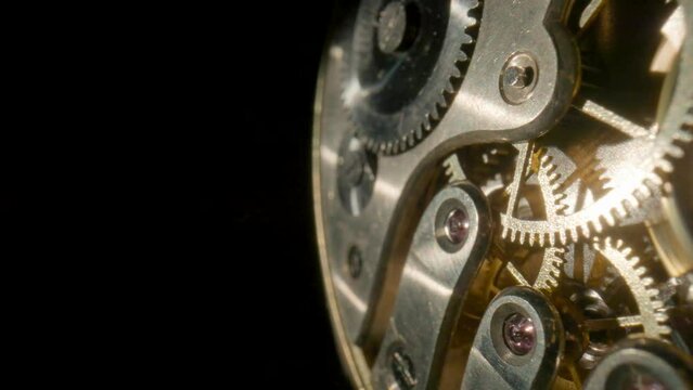 Macro shot of gold internal parts of antique pocket watch. Clockwork with rotating spring, gears, cogwheel and wheels with tootheds on isolated black studio background. Disassembled silver retro watch