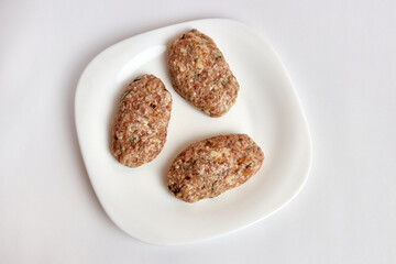 Raw cutlets from minced meat on a white plate.