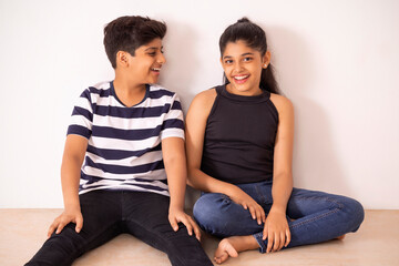 Cheerful boy and girl sitting together on floor against white wall