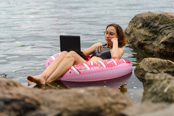 A freelancer works on a laptop while floating on a lake on a rubber ring.