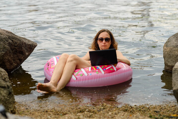 A freelancer works on a laptop while floating on a lake on a rubber ring.