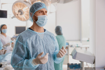 Surgeon in mask and gloves standing in operating room and looking side, ready to work on patient