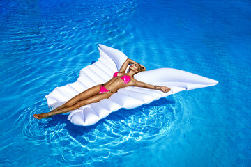 Elegant female model in stylish bikini is lying on a butterfly-shaped mattress in the pool. Sexy...