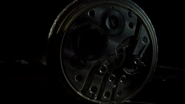 Two antique pocket watches with a working clockwork in darkness and in light on black background. Working clock mechanism with rotating spring, gears, gearing and toothed wheels. Rack focus. Close up.