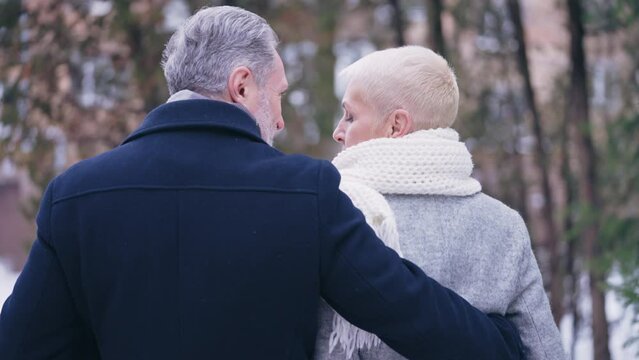 Happy couple in their 50s hugging and walking in winter park, outdoor date, love