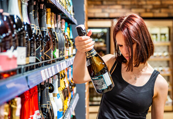 Young woman taking bottle of champagne wine from shelf at supermarket